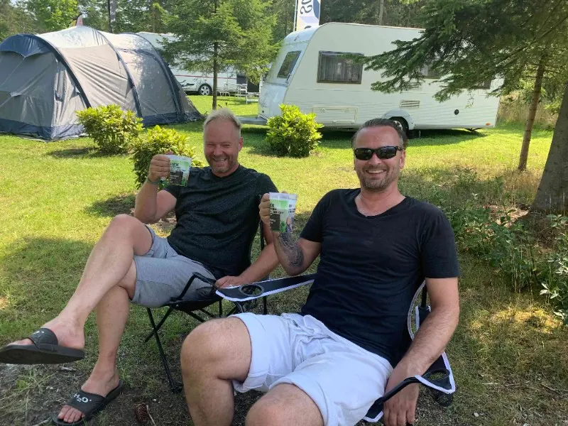 To gæster slapper af i campingstole foran telte og campingvogne.